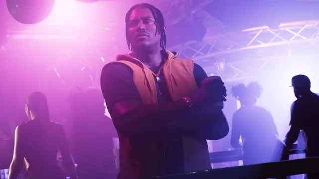 Dre'Quan Priest in an orange vest, arms crossed in a purple-lit club